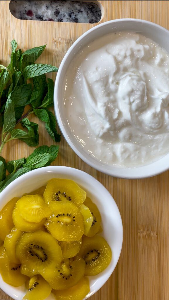 Bowls of kiwi's, nonfat vanilla yogurt, and mint leaves on wooden cutting board